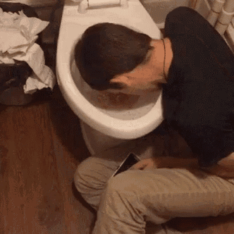 a man is kneeling down next to a toilet with his head in it .