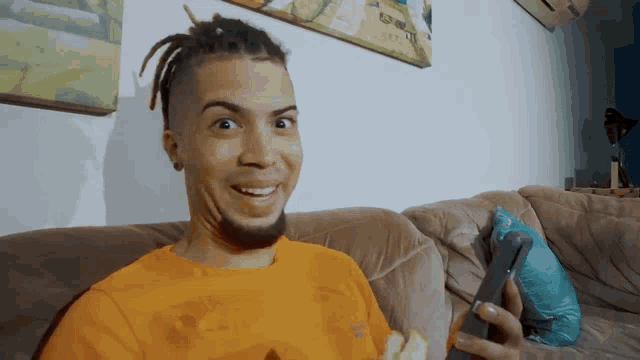 a man with dreadlocks is sitting on a couch holding a cellphone