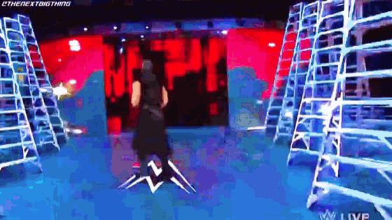 a wrestler is standing on a stage in front of a red wall surrounded by ladders .