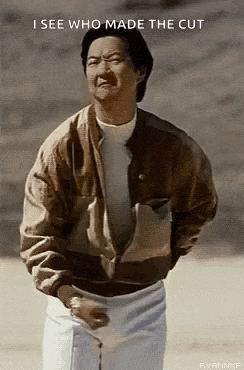 a man in a brown jacket and white shorts is standing in front of a wall and talking .