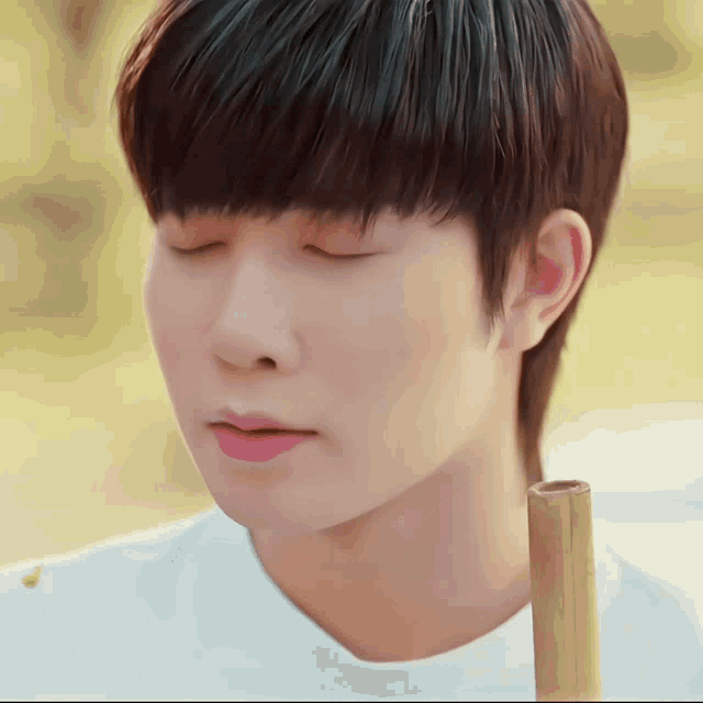 a close up of a man 's face with his eyes closed and a bamboo stick in his hand