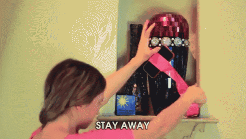 a woman in a pink shirt is putting a pink ribbon around a vase that says " stay away " on the bottom