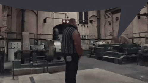 a man in a brown jacket is standing in a factory with a machine .