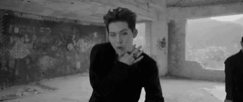 a black and white photo of a man in a black sweater standing in an empty room .