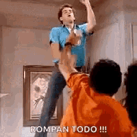 a man in a blue shirt is jumping in the air while another man in an orange shirt holds his hand up .