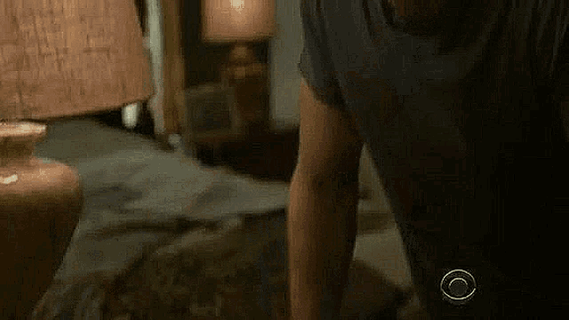 a man in a black shirt is standing in front of a lamp in a bedroom .