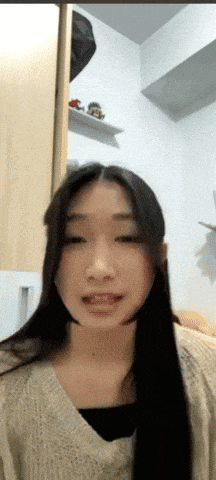 a woman with long black hair and a tan sweater looks at the camera