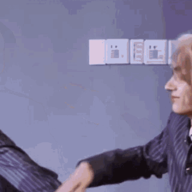 a man is pointing at another man 's head while standing in front of a wall .