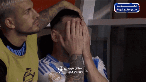 a soccer player is covering his face with his hands while another soccer player looks on
