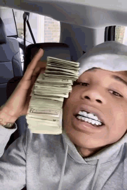 a man in a hoodie is holding a stack of money in his hand .