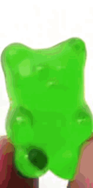 a person is holding a green gummy bear in their hand .