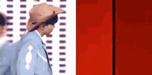 a man in a suit and cowboy hat is standing next to a red wall .
