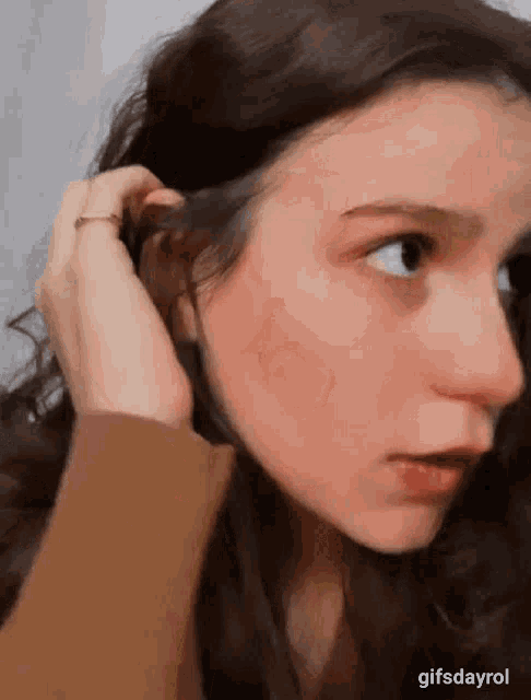 a close up of a woman 's face with her hand on her hair .