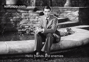 a man in a suit and tie is sitting on a sidewalk next to a fountain .