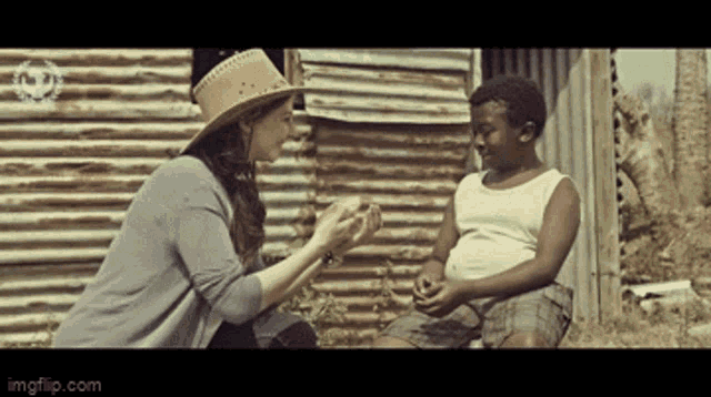 a woman in a cowboy hat is talking to a young boy in a white tank top