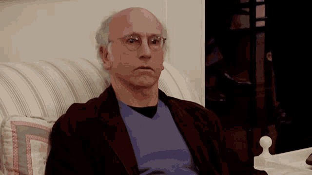 a bald man wearing glasses is sitting on a striped couch