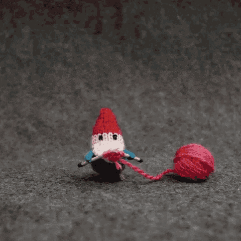 a stuffed gnome is knitting while holding a ball of pink yarn