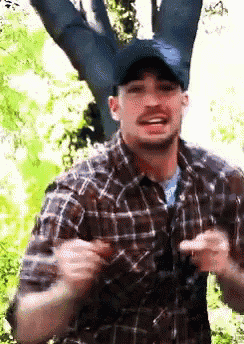 a man wearing a plaid shirt and a hat is standing in front of a tree