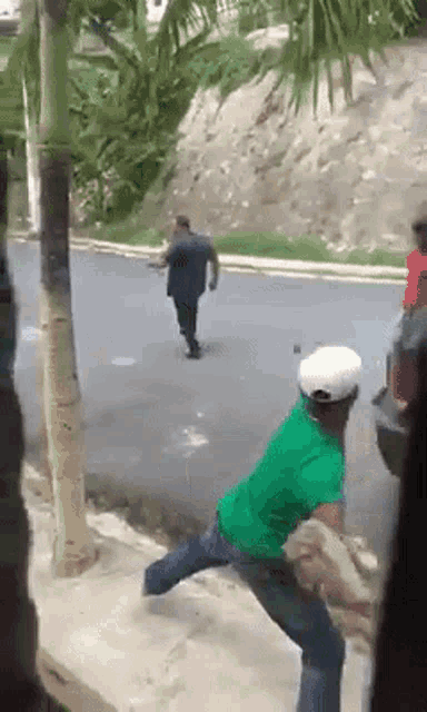 a man in a green shirt is throwing a rock at another man in a white hat