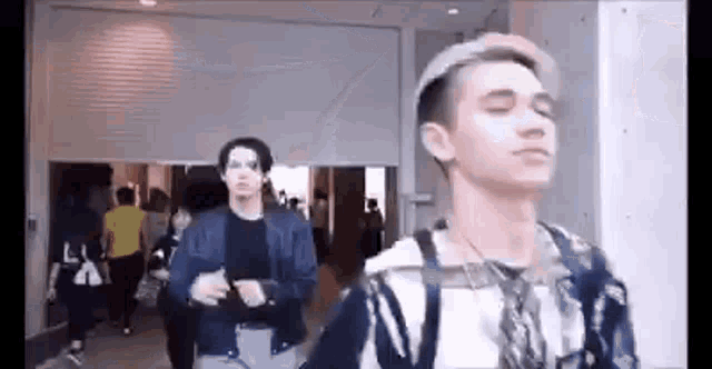 two young men are standing next to each other in a room . one of the men is wearing a hat .
