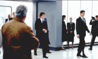 a man in a brown jacket stands in front of a group of people in suits