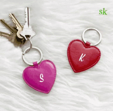a pink heart shaped keychain with the letter s on it and a red heart shaped keychain with the letter k on it .