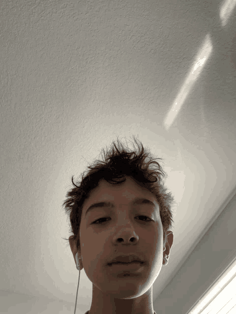 a young boy wearing ear buds looks up at the ceiling