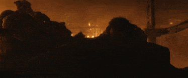 a man laying on a rock in a dark room with a fire in the background