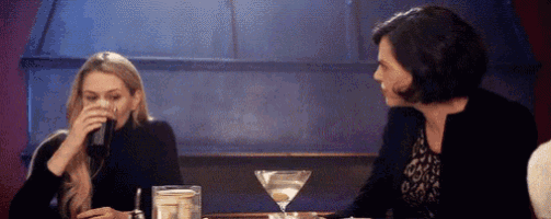 two women are sitting at a table drinking martini 's and talking .