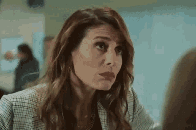 a woman in a plaid jacket and red lipstick is talking to another woman in a room .