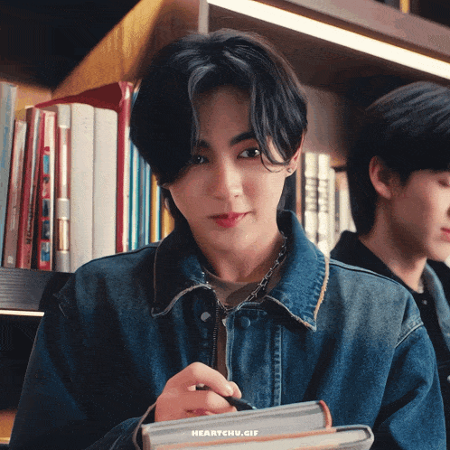 a young man in a denim jacket is holding a pen and a notebook with the words heartchu.gif below it