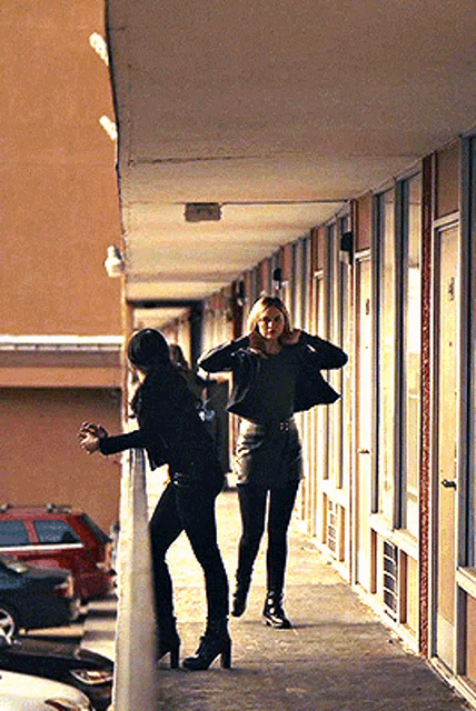 two women are walking down a hallway in front of motel rooms