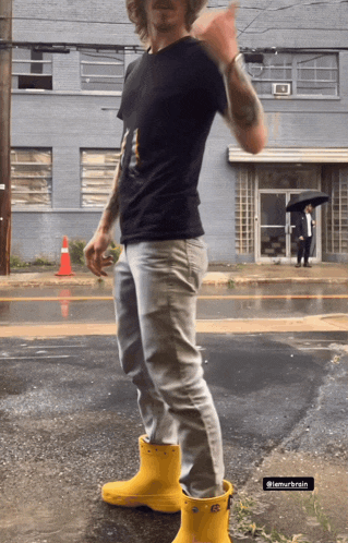 a man wearing a black shirt and yellow rain boots stands in the rain