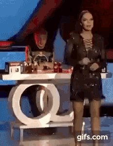 a woman in a black dress is standing in front of a table with a white letter q .