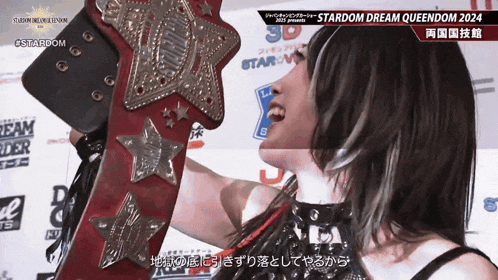 a female wrestler holds up a stardom dream queendom 2024 championship belt