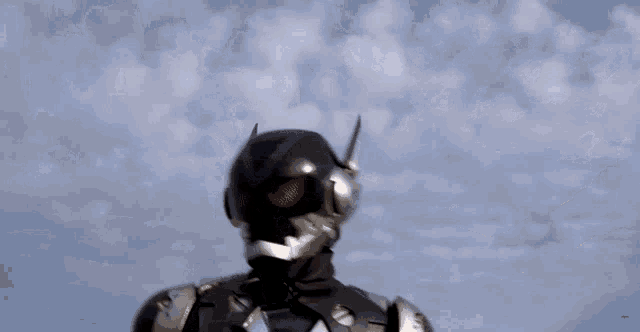a man in a black and silver costume with a helmet that has a horn on it is standing in front of a cloudy sky