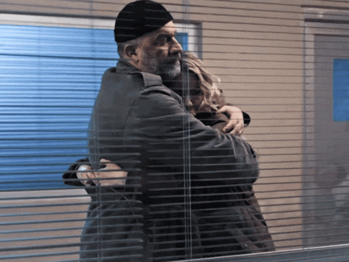 a man and a woman hugging in front of a window