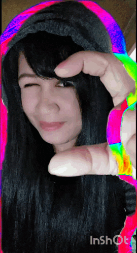 a woman is making a heart shape with her fingers while wearing a rainbow colored hoodie