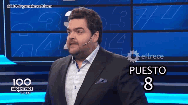 a man in a suit stands in front of a screen that says 100 argentinas dicen