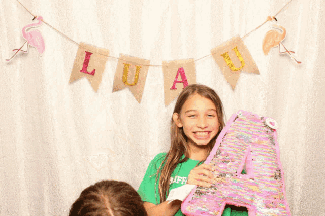 a girl with glasses holds a baby in front of a banner with luau on it