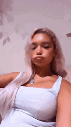 a woman in a white tank top is taking a selfie .