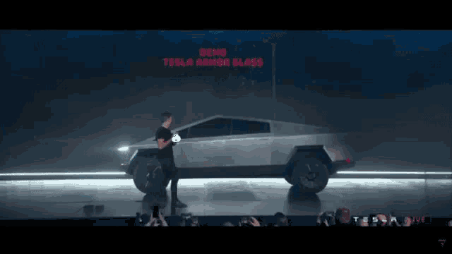 a man is standing next to a tesla car with a sign that says demo tesla armor glass