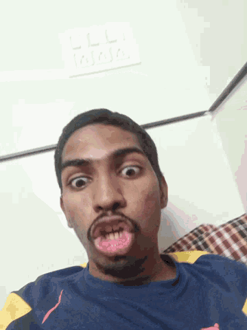 a man is making a funny face in front of a wall with a few electrical outlets