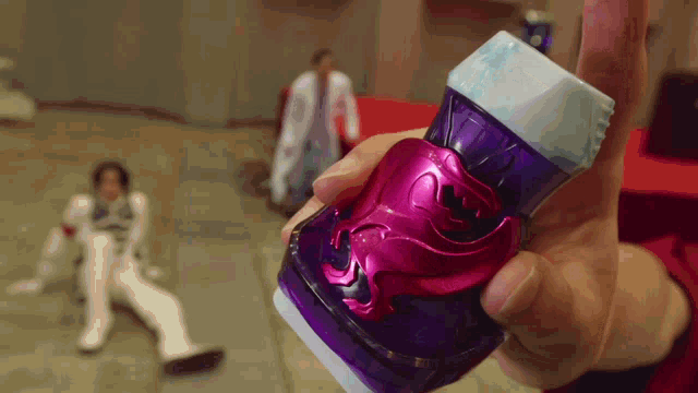 a person is holding a purple object in their hand with a man in a white suit in the background