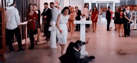 a man in a suit is sitting on the floor at a party while a woman in a white dress stands behind him .