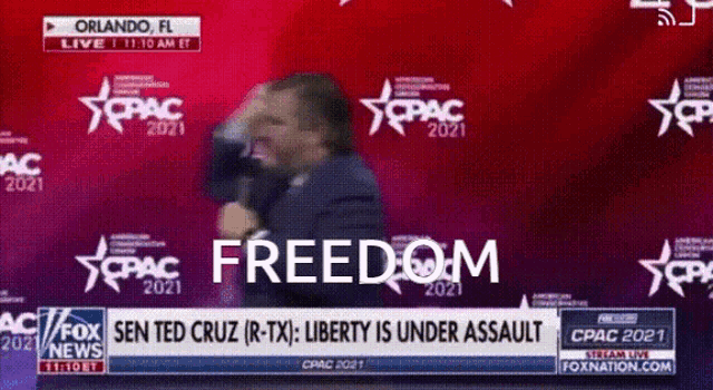 a man is speaking into a microphone in front of a wall that says freedom