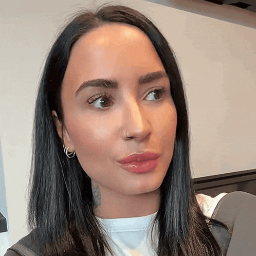 a woman with a nose ring and hoop earrings looks at the camera