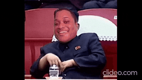 a man in a suit is sitting in a stadium with a red face .