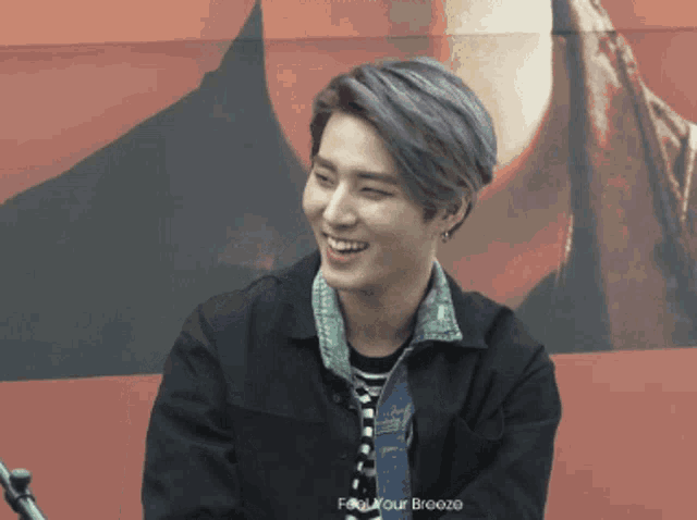 a man with purple hair is smiling in front of a sign that says feel your breeze