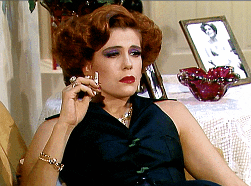 a woman with red hair is smoking a cigarette in front of a picture of a woman